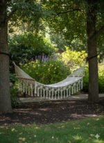 Macrame hammock tied between two trees in a shaded garden
