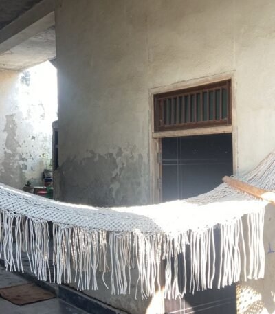 Macrame hammock with wooden spreader bars and long fringes hanging indoors