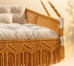 Close-up of mustard macrame sofa swing showing diamond knot pattern, fringe and tufted seat cushion