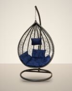 Black HDPE wicker hanging egg chair swing with stand and navy blue cushions, studio background