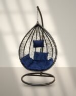 Black HDPE wicker hanging egg chair swing with stand and navy blue cushions in sunlight