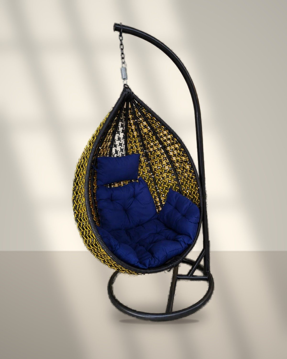 Black and yellow HDPE wicker hanging egg chair swing with stand and navy blue cushions in sunlight