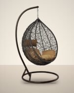 Brown HDPE wicker hanging egg chair swing with stand and tan cushions, studio background