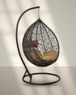 Brown HDPE wicker hanging egg chair swing with stand and tan cushions in sunlight