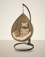 Gold and black HDPE wicker hanging egg chair swing with stand and beige cushions, studio background