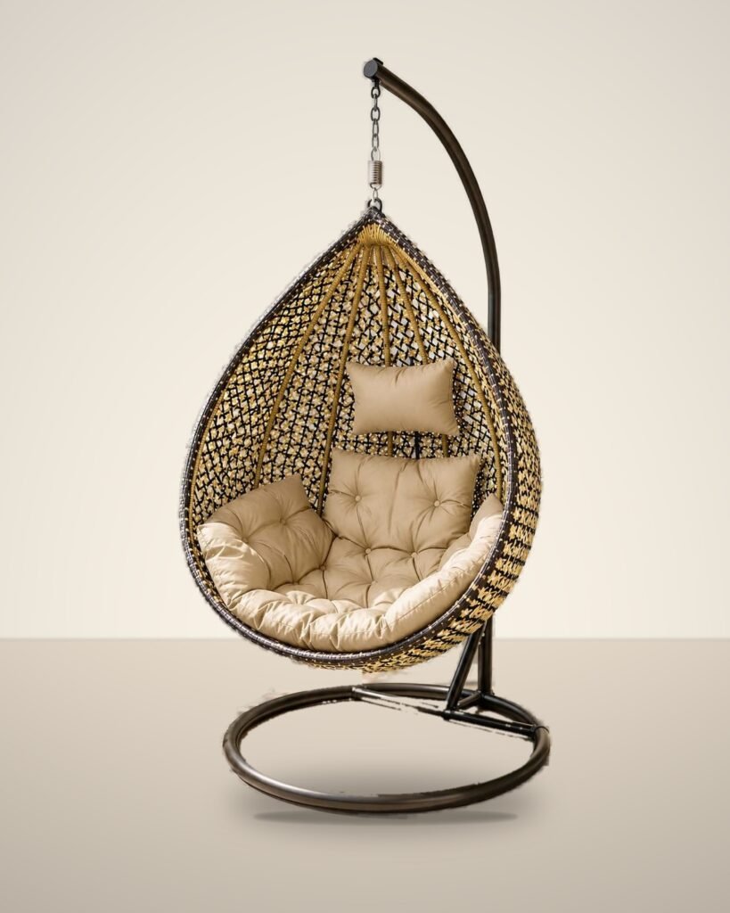 Gold and black HDPE wicker hanging egg chair swing with stand and beige cushions, studio background