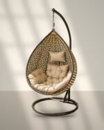Gold and black HDPE wicker hanging egg chair swing with stand and beige cushions in sunlight
